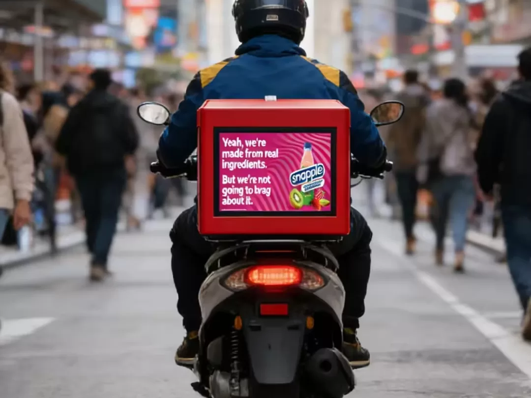 Delivery rider on a scooter with an LED ad box showing a Snapple ad, an example of moving digital OOH advertising in Dubai